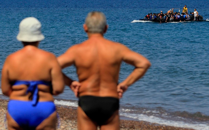 Kupači posmatraju izbjeglice iz Sirije koji su iz Turske pristigli na obale gradića Mitilinija na Grčkom ostrvu Lesvos...