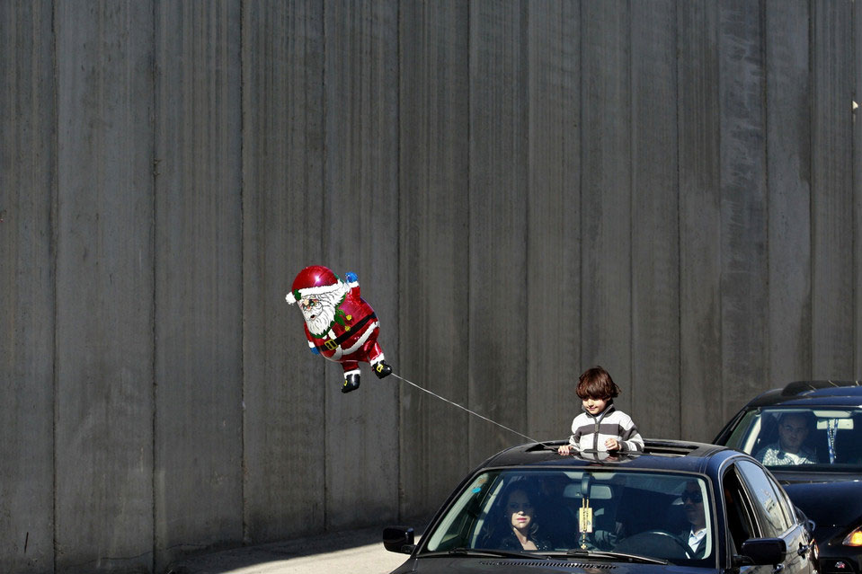 Dječak u automobilu drži Djeda Mraz balon  na Zapadnoj obali u gradu Vitlejemu tokom božićnih proslava..